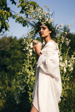 Foto de Una joven en un vestido blanco y una corona de margaritas sostiene en sus manos un pequeño chiken, sobre el fondo del bosque, la luz del atardecer. Concepto de libertad - Imagen libre de derechos