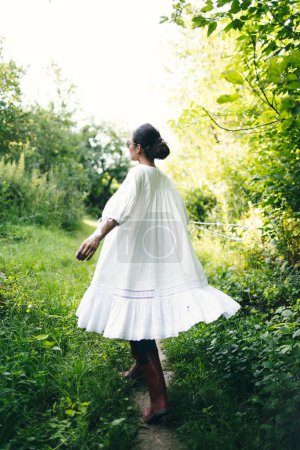 Photo for Beautiful young Indian woman smelling flower in the park, wearing white dress. - Royalty Free Image