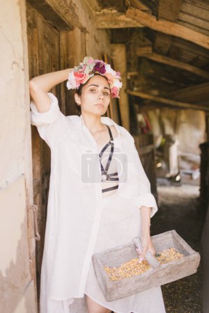 Foto de Hermosa mujer india con un vestido blanco y una corona en la cabeza sostiene una canasta con maíz. La granja o el campo. - Imagen libre de derechos