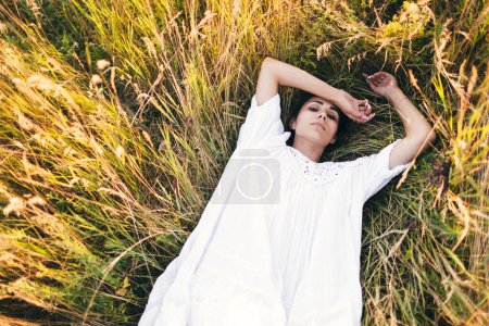 Téléchargez les photos : Conçu Belle jeune femme allongée dans l'herbe, portant une robe blanche. Nature, vacances d'été, vacances et concept de personnes - en image libre de droit