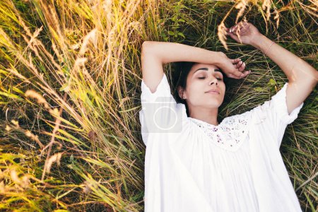 Téléchargez les photos : Conçu Belle jeune femme allongée dans l'herbe, portant une robe blanche. Nature, vacances d'été, vacances et concept de personnes - en image libre de droit
