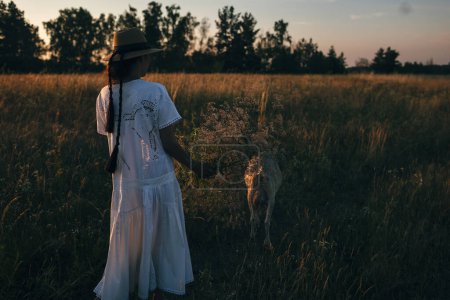 Téléchargez les photos : Une jeune femme sur le terrain marche avec des chèvres. La fille et les chèvres dans la prairie en été. L'amour pour les animaux. Une ferme de chèvres. Les animaux. Une femme heureuse avec un animal. Bonté et amour pour les animaux - en image libre de droit