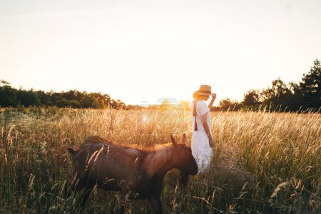 Photo for Summer delight and travel. Young carefree female in rustic linen cloth relaxing in summer meadow. Stylish boho woman with straw hat posing among wildflowers in sunset light. Atmospheric moment - Royalty Free Image