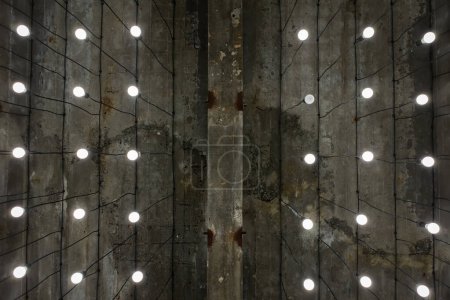 Ampoules à ton blanc allumées dans les lampes alignées sous un plafond en ciment peint gris - style rustique et loft - espace ouvert - vue perspective vers.