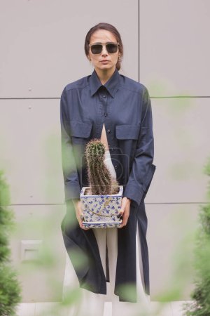 Téléchargez les photos : Femme tendrement debout en kimono avec du cactus dans les mains sur fond gris. La fille porte séduisante sa robe. Détails à la mode du kimono sur fond gris - en image libre de droit