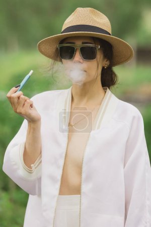 Téléchargez les photos : Belle femme fumant cigarette électronique dans la rue. - en image libre de droit
