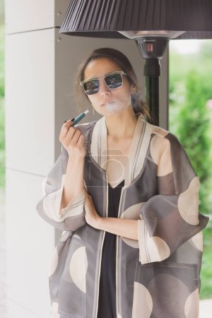Téléchargez les photos : Belle femme fumant cigarette électronique dans la rue. - en image libre de droit