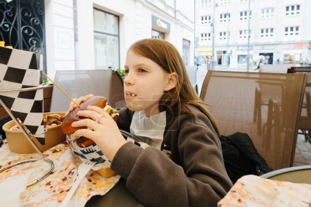 Foto de Elegante chica hipster comiendo hamburguesa jugosa. Chica mordiendo deliciosa hamburguesa con queso en la cafetería de la calle. Verano. picnic de vacaciones de verano. espacio para texto - Imagen libre de derechos