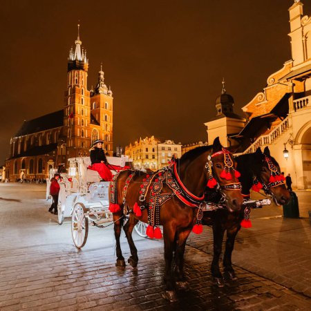 Téléchargez les photos : Cracovie, Pologne - 24 mai 2023 : Voitures pour les touristes à cheval sur le fond de la cathédrale Mariacki à la place principale dans la vieille ville. - en image libre de droit