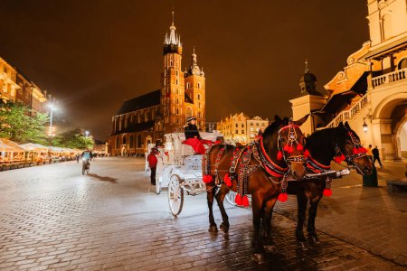 Téléchargez les photos : Cracovie, Pologne - 24 mai 2023 : Voitures pour les touristes à cheval sur le fond de la cathédrale Mariacki à la place principale dans la vieille ville. - en image libre de droit