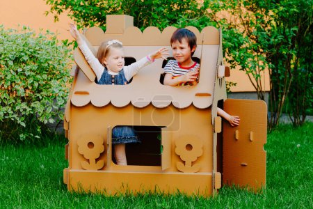 Photo for Children are playing in cardboard kid house. Child having fun outdoors - Royalty Free Image