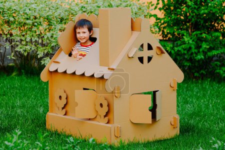 Photo for Children are playing in cardboard kid house. Child having fun outdoors - Royalty Free Image