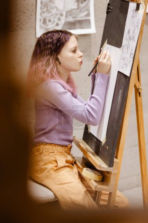 Téléchargez les photos : Fille 11 ans artisan peignent sur toile en atelier debout devant le chevalet. Portrait d'une fille peignant lors d'un cours d'art - en image libre de droit