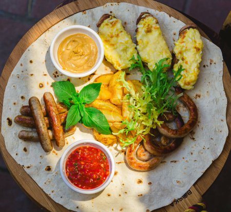 Photo for German style grilled sausages with potato wedges and bread with cheese and sauces close-up on a wooden tray on the table. Shallow dof - Royalty Free Image