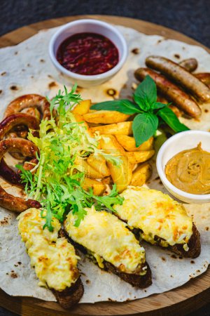 Photo for German style grilled sausages with potato wedges and bread with cheese and sauces close-up on a wooden tray on the table. Shallow dof - Royalty Free Image
