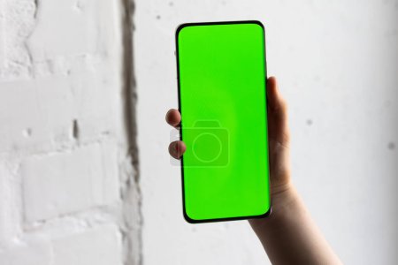 Foto de Imagen burlona de una persona que sostiene un teléfono móvil inteligente con pantalla verde en blanco - Imagen libre de derechos
