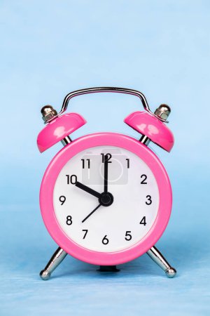 Foto de Reloj despertador rosa sobre fondo azul. Ahorre tiempo, ahorro de luz natural. - Imagen libre de derechos