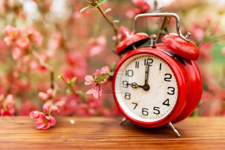 Foto de Pink flowers and retro red alarm clock. Spring forward, springtime or daylight savings time background. - Imagen libre de derechos