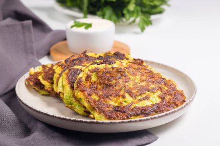 Vegetarian zucchini fritters or courgettes pancakes, served with fresh herbs and sour cream.