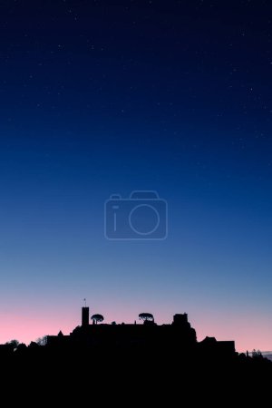 Dawn breaking over the silhouette of the medieval village of Turenne in the Correze department of France with stars overhead