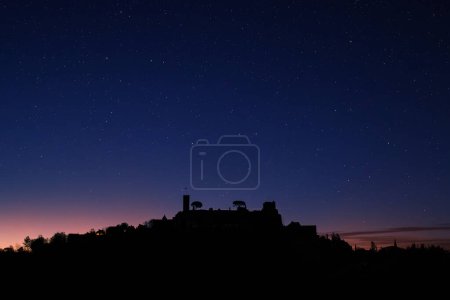 Star filled night sky over the silhouetted medieval village of Turenne in the Correze department of France