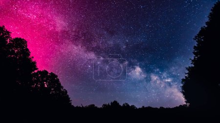 Cielo nocturno lleno de estrellas y la Vía Láctea iluminado por las brillantes magentas de la Aurora Boreal sobre la región de Dordoña de Francia