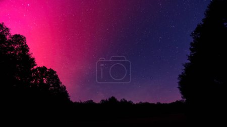 Cielo nocturno lleno de estrellas iluminado por las brillantes magentas de la Aurora Boreal sobre la región de Dordoña de Francia