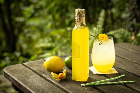 Citronnelle citron citron citron limonade maison dans une bouteille et un verre avec décoration fruitée sur table en bois dans la nature