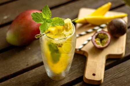 Hausgemachte Mango-Passionsfrucht-Limonade im Glas mit Obst und Dekoration auf Holztisch in der Natur