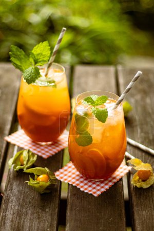 Peach homemade lemonade in a glass with fruit and decoration on wooden table in nature