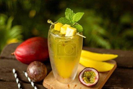 Mango passionfruit homemade lemonade in a glass with fruit and decoration on wooden table in nature