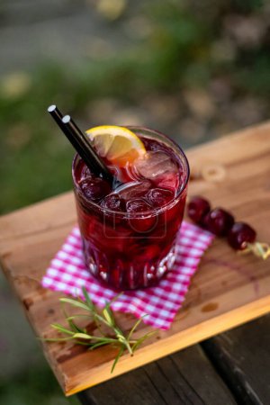 Cherry homemade lemonade in a glass with fruit and decoration on wooden table in nature
