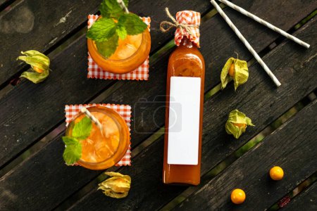 Limonada casera de albaricoque en una botella de vidrio con fruta y decoración en mesa de madera en la naturaleza