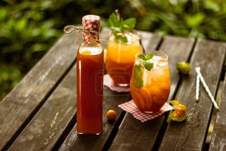 Apricot homemade lemonade in a glass bottle with fruit and decoration on wooden table in nature