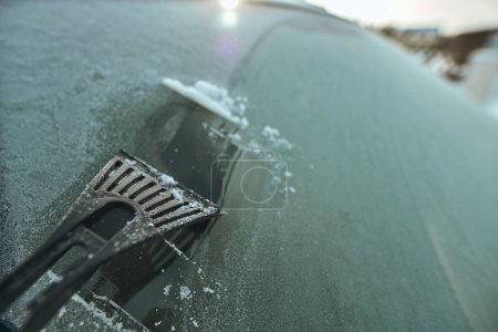 Photo for Cleaning the windshield from ice with a plastic ice scraper. - Royalty Free Image