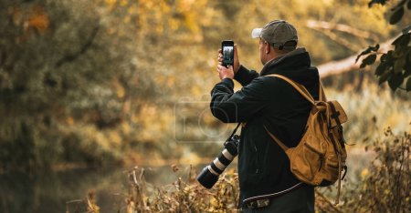 Man taking photo outdoors. Pro photographer taking landscape and wildlife pictures. Big camera