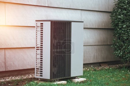 Photo for An air conditioner outdoor unit outside of a house in the grass. Modern HVAC and heat pump system - Royalty Free Image
