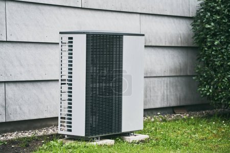 Téléchargez les photos : Un climatiseur extérieur à l'extérieur d'une maison dans l'herbe. Système moderne de climatisation et de pompe à chaleur - en image libre de droit