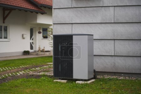 Téléchargez les photos : Un climatiseur extérieur à l'extérieur d'une maison dans l'herbe. Système moderne de climatisation et de pompe à chaleur - en image libre de droit