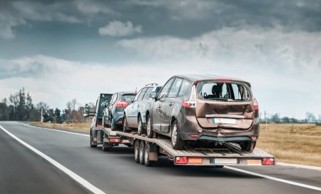 Photo for Emergency roadside assistance on the highway. side view of the fltabed tow truck with a damaged vehicles after a traffic accident. - Royalty Free Image