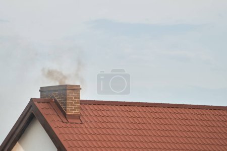 El humo oscuro sale de la chimenea de una casa moderna en invierno. Calefacción con combustible sólido. El concepto de contaminación ambiental