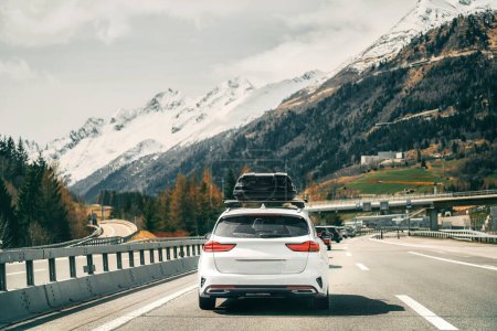 Photo for Rooftop cargo carrier bag. Rear view of a car with a roof box. Alpine highway. Black Roof Box on a Sporty White Wagon Family Car. Removable black car trunk for luggage on the roof of a car. - Royalty Free Image