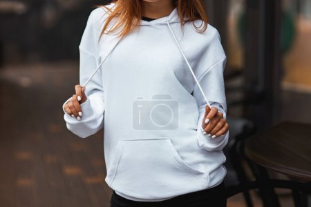 Die Frau trägt einen weißen Kapuzenpullover. Der freie Raum auf ihrer Bluse ist für Logodesign und Branding-Kleidungsattrappen. Einfache Sweatshirt-Vorlage.