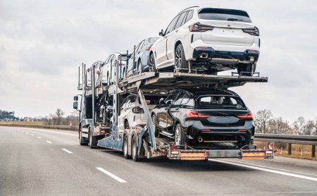 Autotransporter transportiert neue Luxusfahrzeuge über die Autobahn, Rückansicht des Anhängers. Großer Autotransporter mit neuen deutschen Sportwagen, der zum Händler geliefert wird. LKW mit neuen leistungsstarken neuen Fahrzeugen.