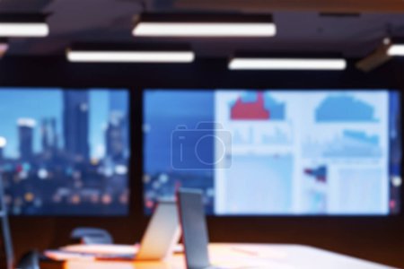Photo for Blurred office background. Modern Empty Meeting Room with Big Conference Table with Various Documents and Laptop on it. Wall TV Showing Company Statistics, Graphs. Late Evening or Night City Outside. - Royalty Free Image