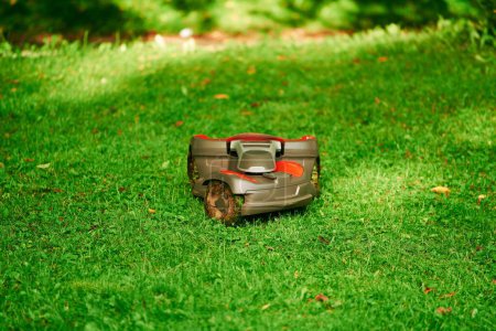 Téléchargez les photos : Tondeuse automatique en action. Robot tondeuse à gazon. dans le jardin d'herbe. Maison intelligente et vie - en image libre de droit