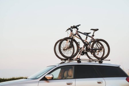 Foto de Coche de pasajeros con dos bicicletas montadas en el techo. Bicicletas de techo. Transporte de material deportivo. - Imagen libre de derechos