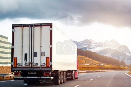 Foto de Camión de carga en las montañas. Camión de carga de reparto en la autopista Europa. Concepto de entrega global. En el camino a la entrega - Imagen libre de derechos