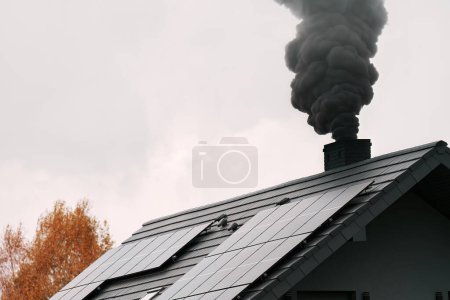 Photo for A modern house emits black smoke from its chimney in winter, causing environmental pollution and global warming. Black smoke from  chimney of a house in the countryside shows the impact of heating. - Royalty Free Image