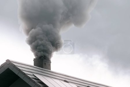 Photo for Dark smoke comes out of the chimney of a modern house during the late autumn and winter. Heating with solid fuel. The concept of environmental pollution - Royalty Free Image